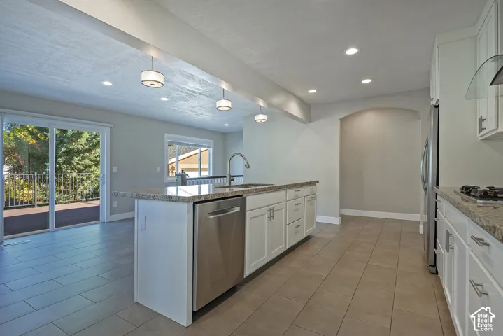 Kitchen featuring a center island with sink, stainless steel appliances, white cabinetry, and granite countertops