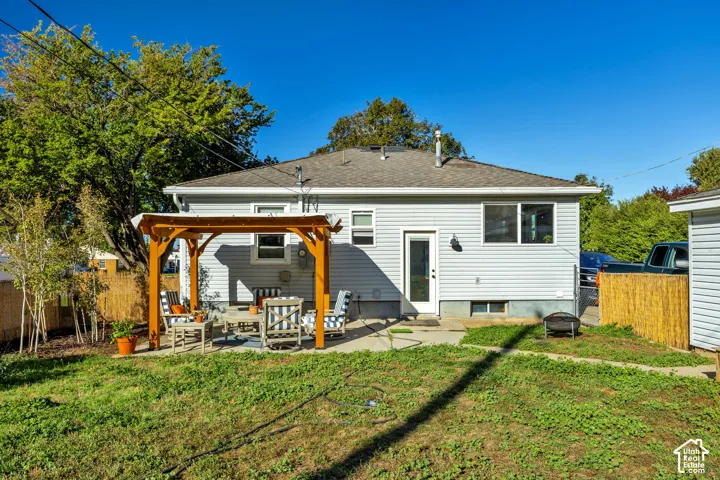 Rear exterior with light gray siding, a wood pergola, a concrete patio, and a grass lawn