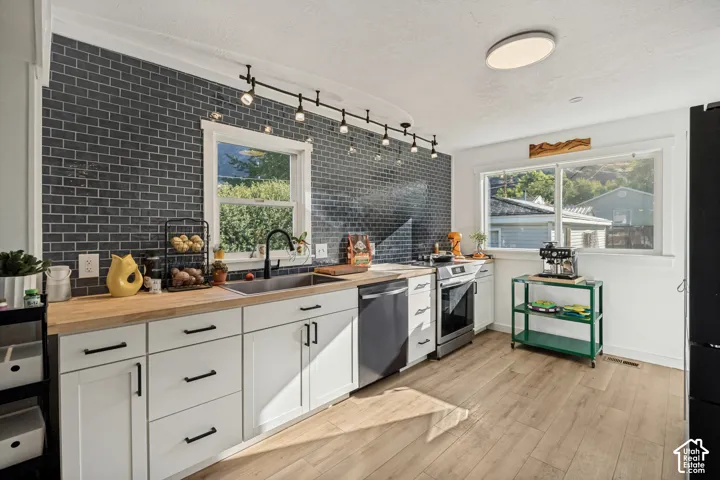 Kitchen featuring wood-finish flooring, white cabinetry with matte black hardware, wood-finish countertops, subway tile backsplash, and a stainless steel sink with a matte black faucet