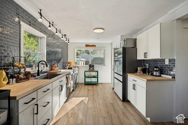Kitchen featuring wood-finish flooring, white cabinetry with black hardware, wood countertops, and full-height dark subway tile backsplash