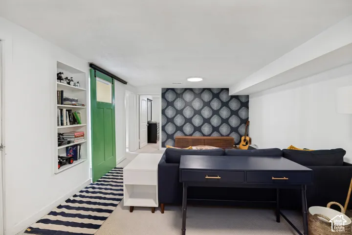 Built-in shelving, green barn door, accent wall with patterned wallpaper, recessed lighting, and light-colored flooring