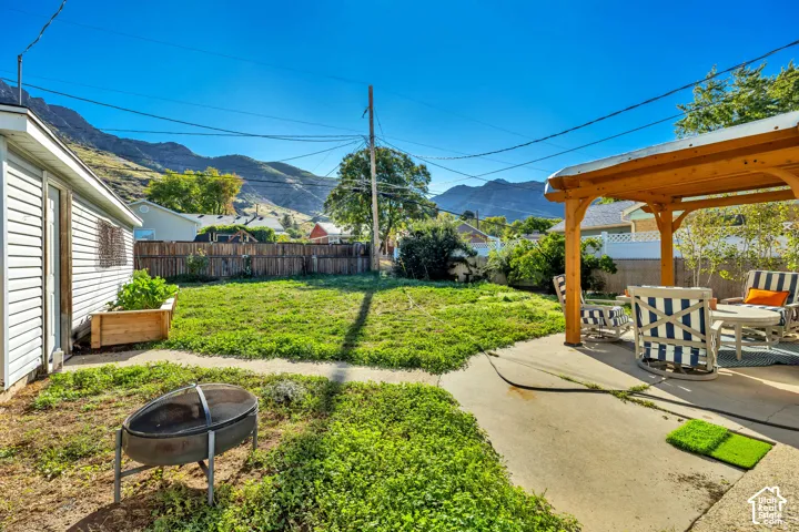 Concrete patio with a wood pergola, expansive lawn, and raised garden bed