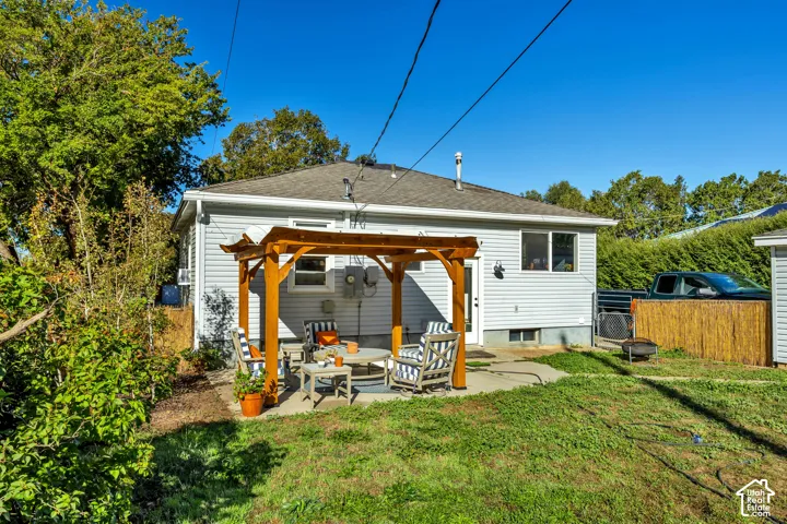 Rear exterior featuring light gray siding, a wood pergola on a concrete patio, and a shingle roof