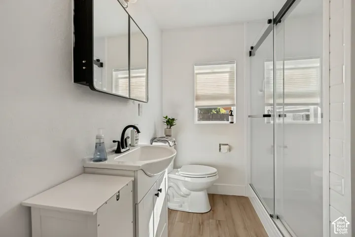 Vanity with integrated sink, black-framed medicine cabinet, glass-enclosed shower with black hardware, and wood-finish flooring