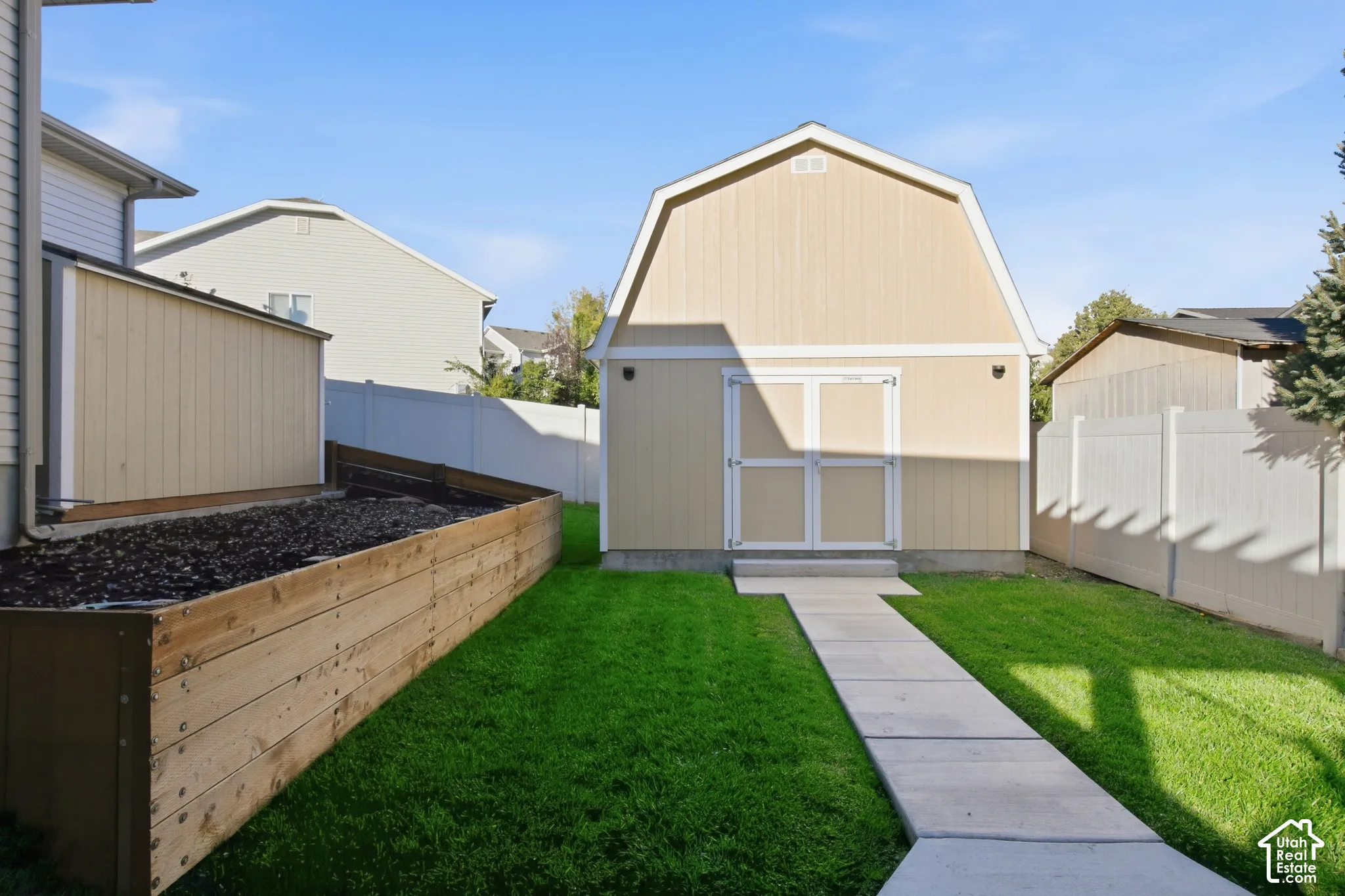 Expansive backyard featuring a manicured lawn, concrete pathway, large storage shed with double doors, and a raised planter box