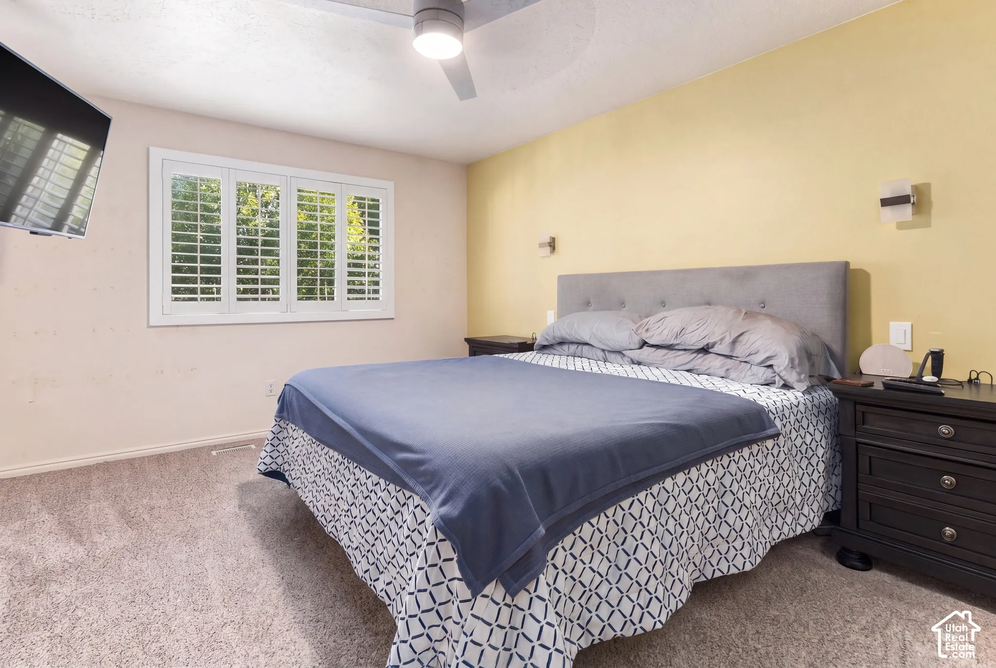 Window with white plantation shutters, carpeted flooring, ceiling fan, and wall-mounted sconce lighting