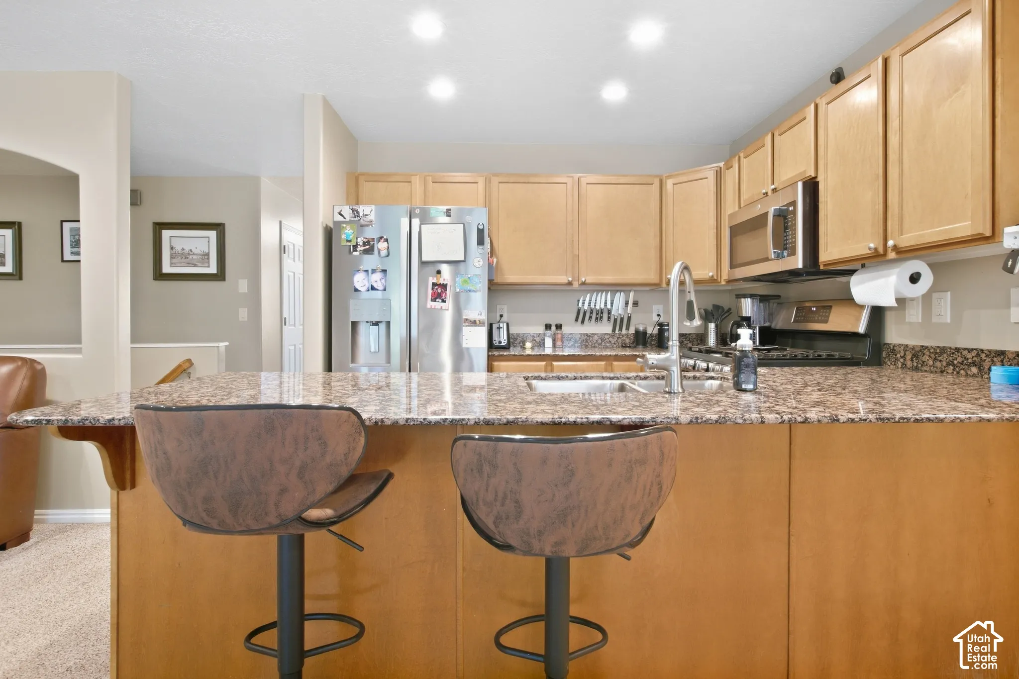 Kitchen featuring granite countertops, stainless steel appliances, wood cabinetry, recessed lighting, and a breakfast bar