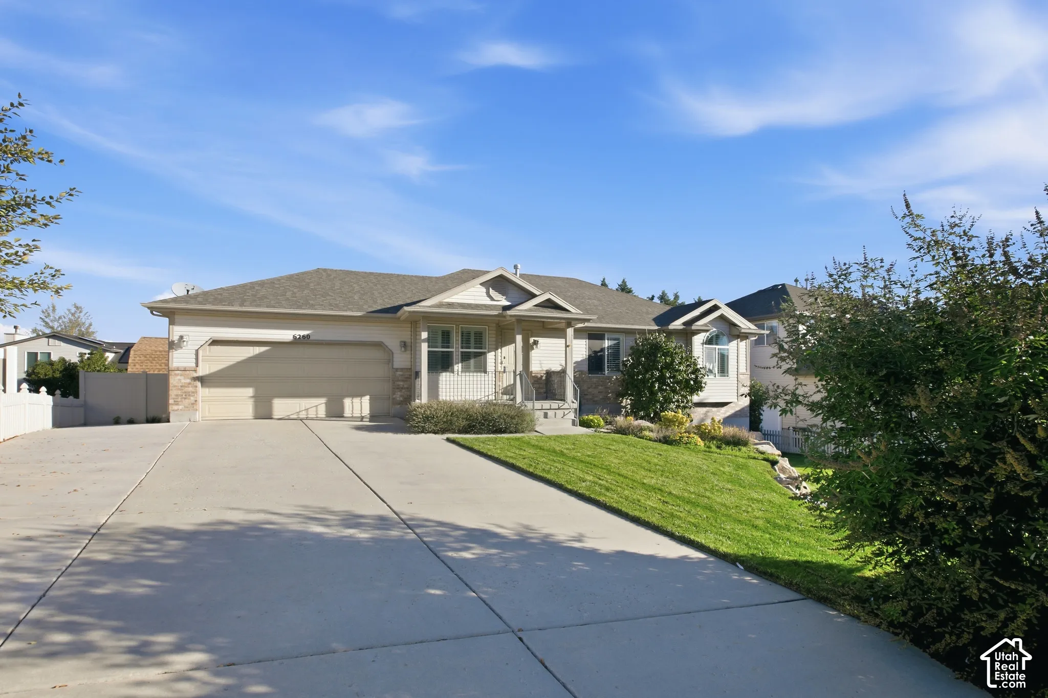 Exterior featuring a light-colored stucco finish, stone accents, attached two-car garage, concrete driveway, and a sloped lawn with mature landscaping