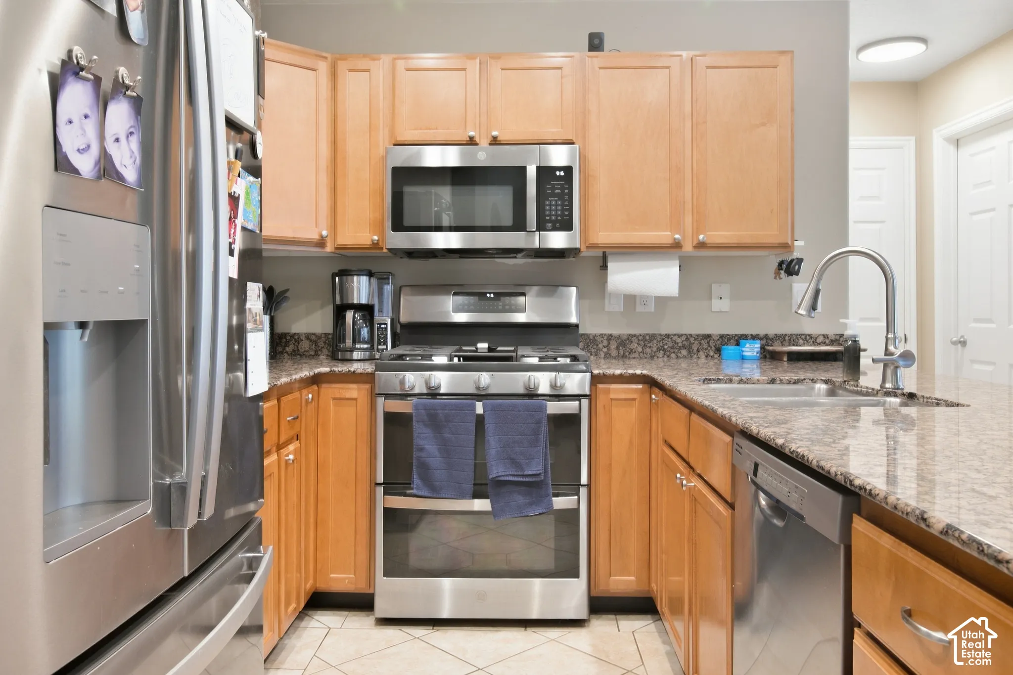 Kitchen featuring stainless steel appliances, wood-finish cabinetry, stone countertops, and tile flooring