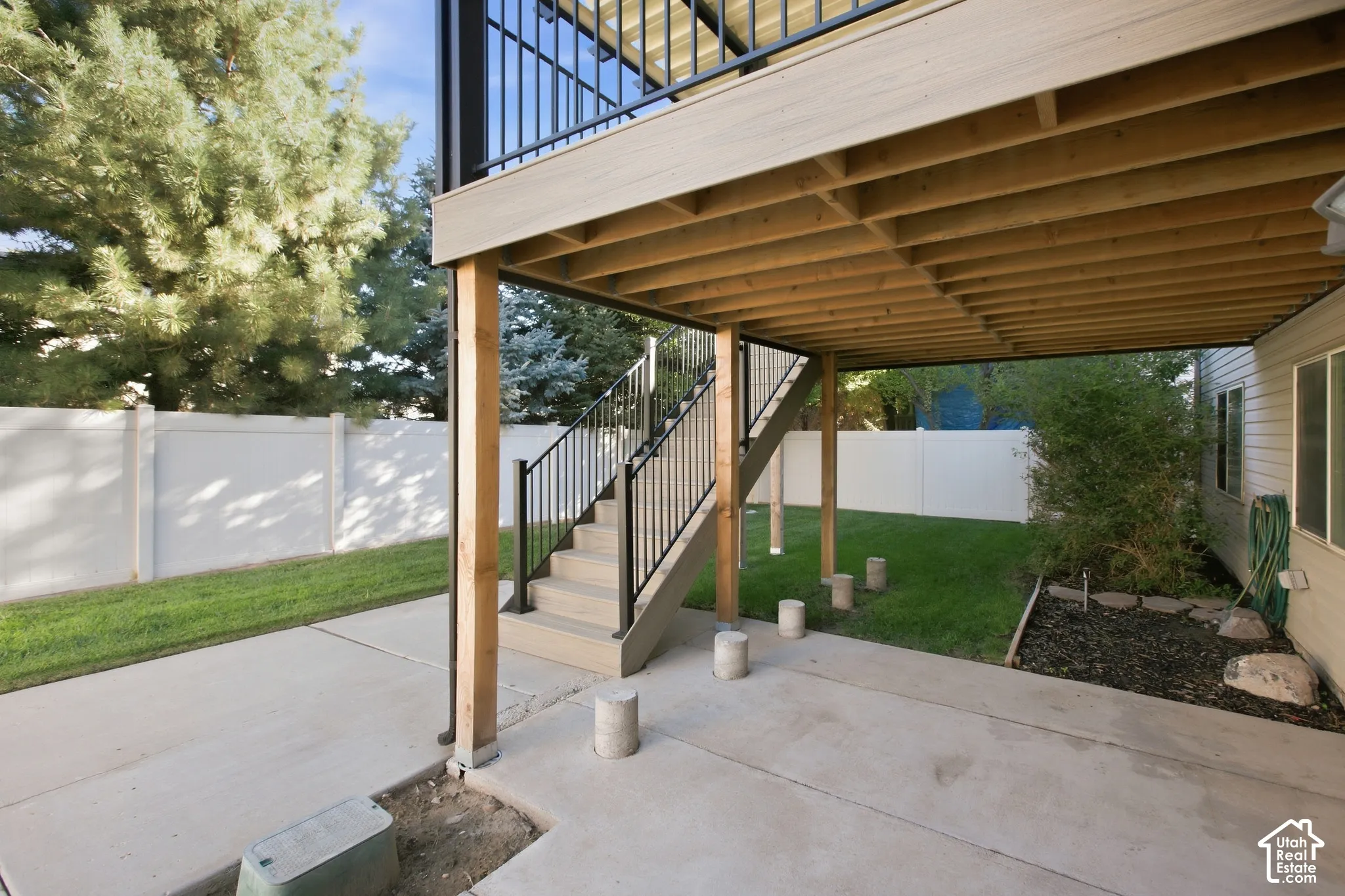 Finished concrete patio with a full privacy fence, leading to a landscaped area and a multi-level deck with stairs