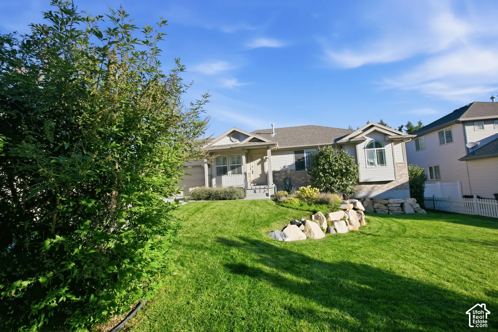 Expansive lawn with mature landscaping, stone retaining wall, and a multi-level exterior with bay window