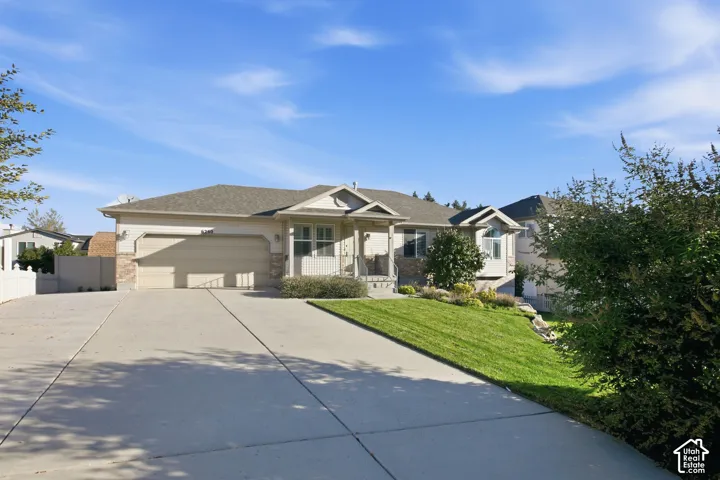 Exterior featuring a light-colored stucco finish, stone accents, attached two-car garage, concrete driveway, and a sloped lawn with mature landscaping