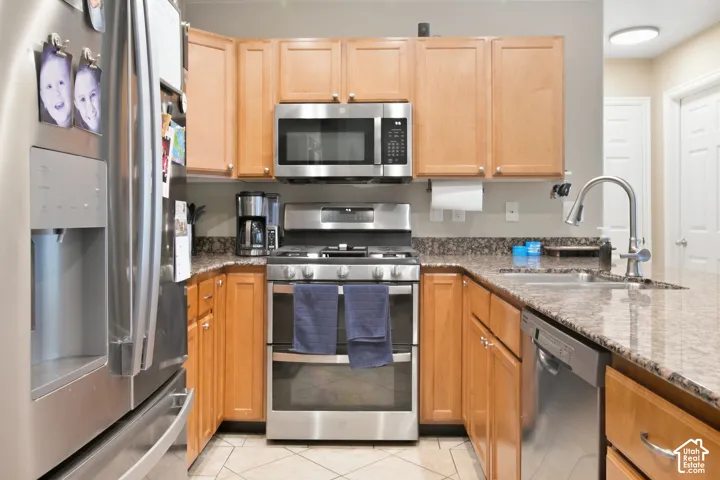Kitchen featuring stainless steel appliances, wood-finish cabinetry, stone countertops, and tile flooring