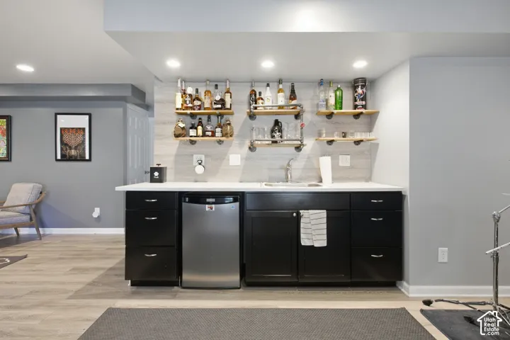 Wet bar featuring black cabinetry, a stainless steel beverage refrigerator, a built-in sink, and open shelving