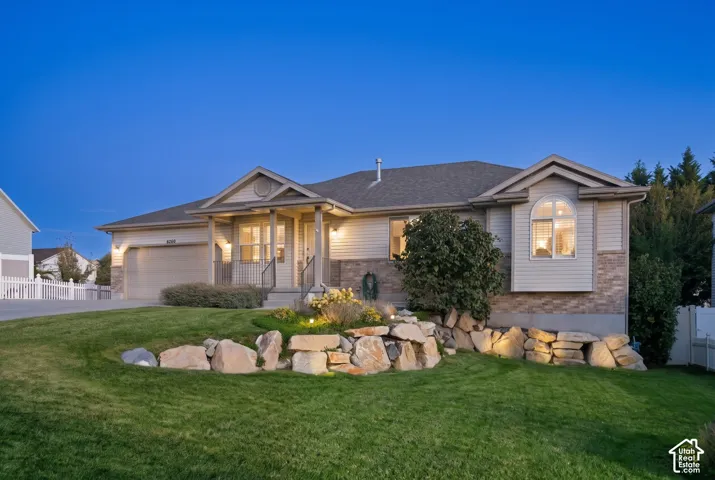 Exterior featuring a stone and siding facade, covered entry, attached garage, and a landscaped front yard with rock retaining walls