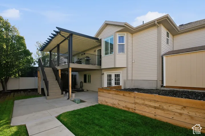 Attached elevated deck with a louvered pergola, concrete patio, dual French doors, and a bay window