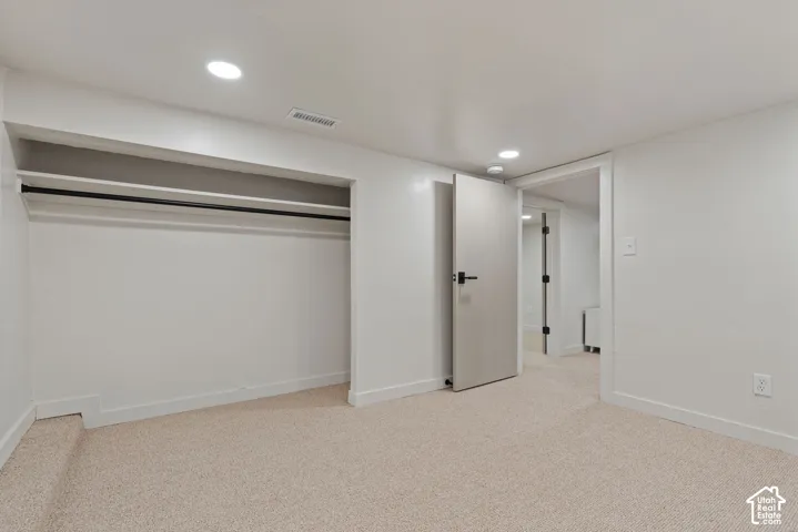 Neutral-toned carpeting, recessed ceiling lighting, a built-in closet with shelving and a hanging rod, and a solid interior door with matte black hardware