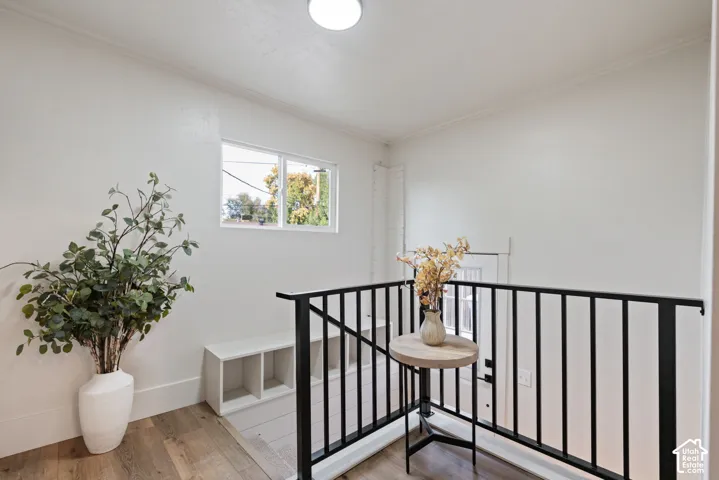 White walls and ceilings, wood-finish flooring, white window trim, black metal railing, and a built-in storage bench