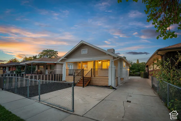 Property exterior featuring a front porch with black railing, a paved driveway, and chain link fencing