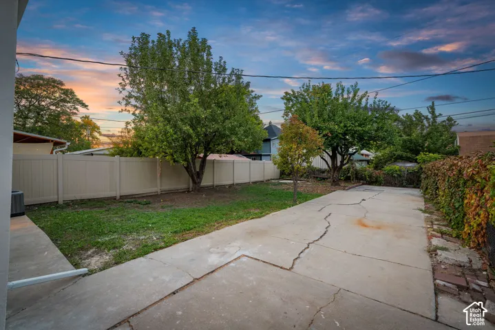 Expansive concrete patio with a manicured lawn, established trees, and perimeter fencing