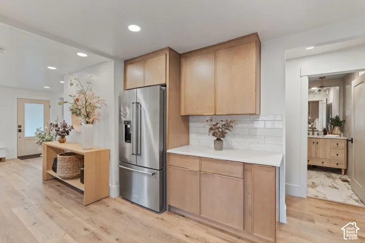 Stainless steel refrigerator, light wood-finish cabinetry, white subway tile backsplash, recessed lighting, and wood-finish flooring