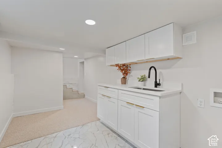 White shaker cabinetry with gold-finish hardware, a single basin sink with a matte black faucet, and a light-toned countertop