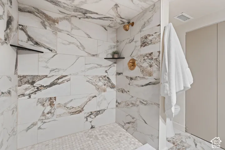 Walk-in shower with large-format tile walls, hexagonal mosaic tile flooring, built-in shelving, and brass-finish fixtures