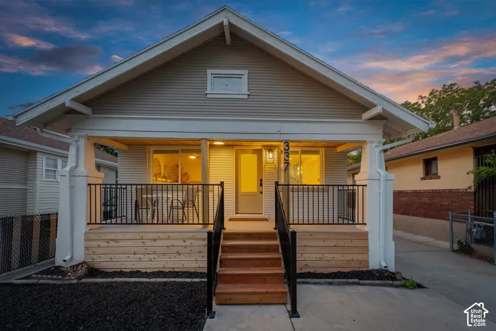 Gable roofline, horizontal siding exterior, covered porch with wood steps, black metal railings, and a prominent front door with an exterior light fixture