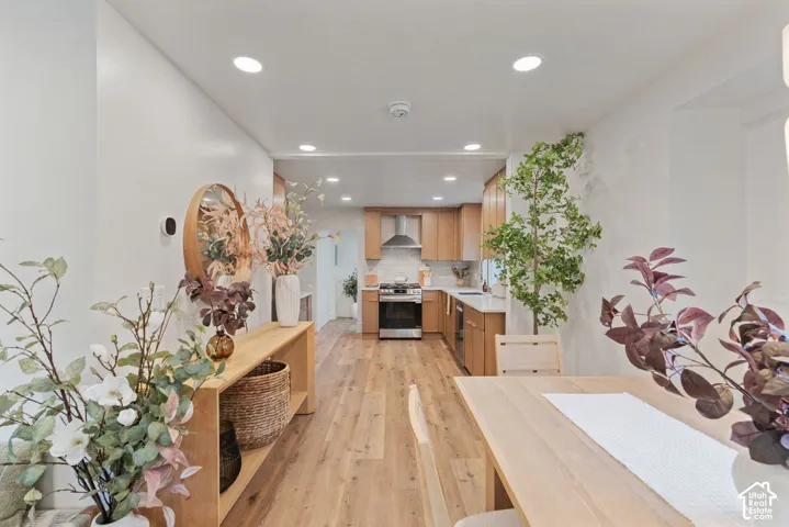 Wood-finish flooring throughout, recessed ceiling lighting, light wood cabinetry, stainless steel range, and a tile backsplash