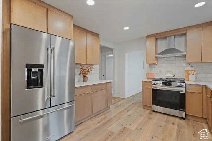 Kitchen featuring wood-finish flooring, light wood cabinetry, stainless steel appliances, white countertops, and a subway tile backsplash
