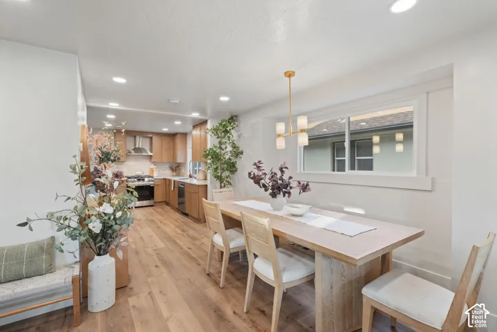 Recessed lighting, wood-finish flooring, kitchen with stainless steel appliances, light wood cabinetry, and a contemporary dining room chandelier