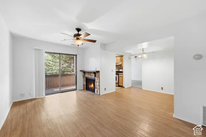 Wood-finish flooring, stone-faced fireplace, sliding glass door, private balcony, and ceiling fan