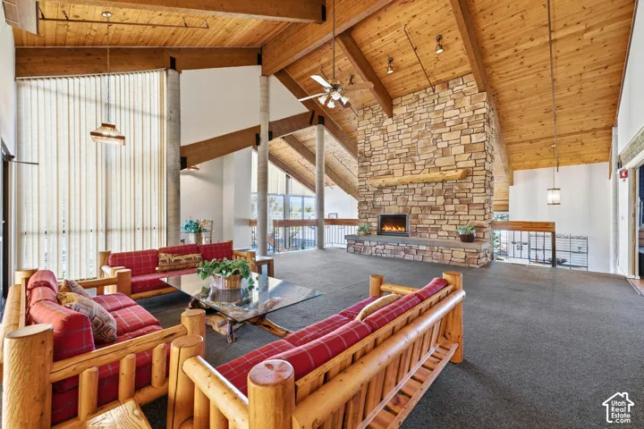 Vaulted wood-paneled ceilings with exposed beams, a stacked stone fireplace with a substantial hearth, vertical blinds on large windows, and a ceiling fan