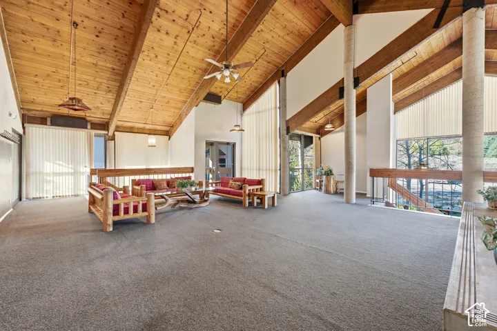 Cathedral wood-paneled ceiling, exposed wood beams, ceiling fans, carpeted flooring, and a wood railing
