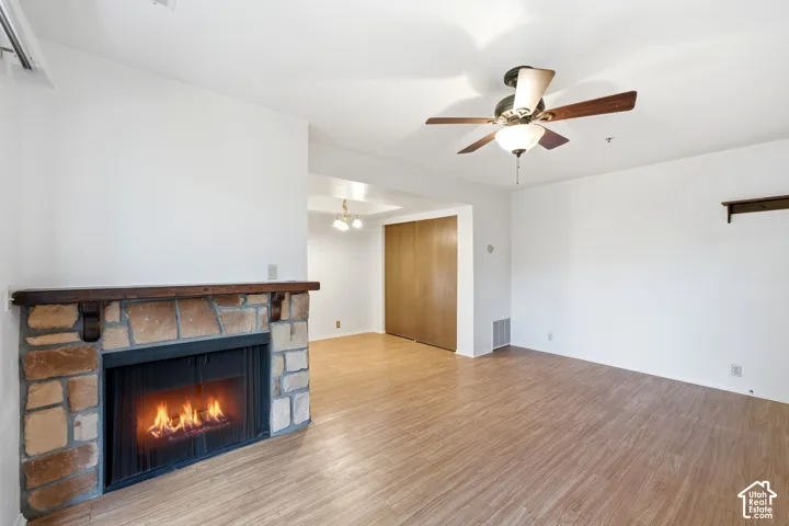 Living area with wood-finish flooring, a stone-surround fireplace, and a ceiling fan with integrated lighting