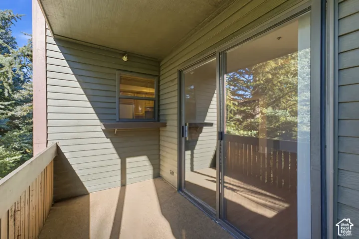 Balcony with concrete flooring and wood railing, featuring a sliding glass door and a fixed window