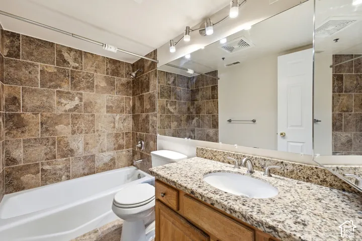 Full tile tub surround, white porcelain bathtub, light wood-finish vanity with an undermount sink, granite-style countertop, and a large wall-mounted mirror