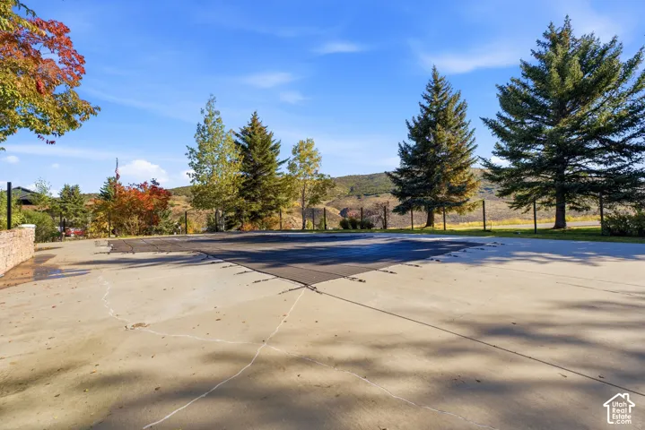 Paved pool deck featuring a covered swimming pool, stone wall, and mature landscaping