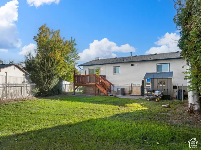 Expansive backyard with a manicured lawn, a wooden deck, a chain link fence, mature trees, and a utility shed