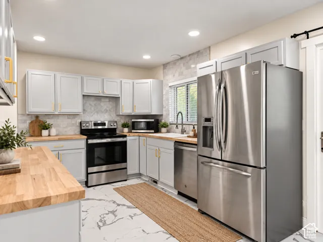 Stainless steel appliance suite, light wood-finish countertops, light gray cabinetry with gold-tone hardware, white marble-pattern flooring, and a tiled backsplash. Virtually Staged