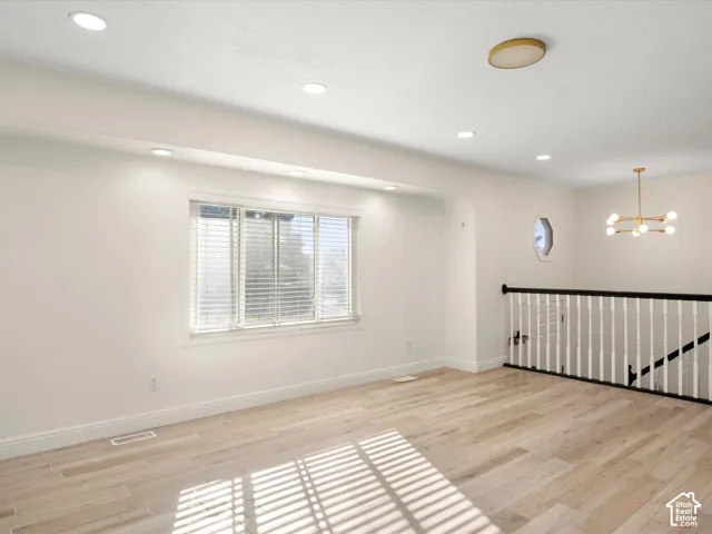 Recessed lighting, wood-finish flooring, staircase with white balusters and dark handrail, modern chandelier, and an octagonal window