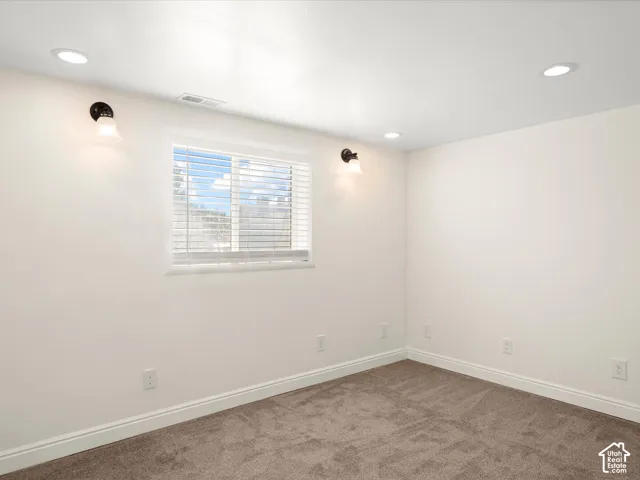 Recessed ceiling lighting, wall-mounted sconces, window with blinds, light-colored walls, and brown carpet flooring