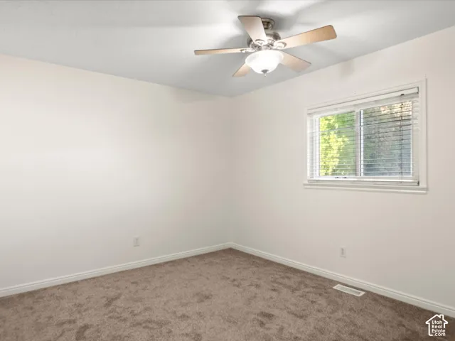 Neutral wall finishes, textured carpeting, a window with horizontal blinds, and a ceiling fan with integrated lighting