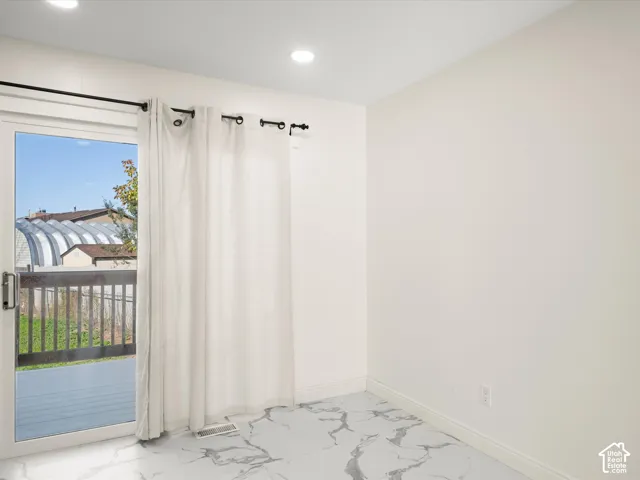 Sliding glass door leading to a deck, white walls, recessed ceiling lighting, and white tile flooring with gray veining