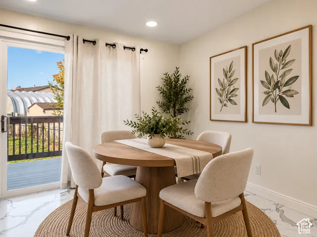 Wood-finish dining table with seating for four, set on a round woven area rug. Virtually Staged