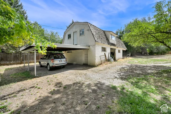 Detached barn structure with dormer, carport, gravel driveway, and expansive yard space