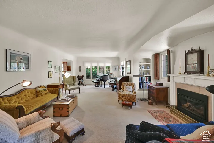 Spacious living area featuring a fireplace with a mantel, built-in shelving, multiple windows, and light-colored carpeting