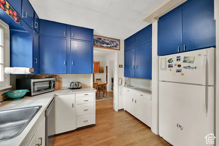 Kitchen featuring blue upper cabinetry, white lower cabinetry, light countertops, a stainless steel sink, and wood-finish flooring