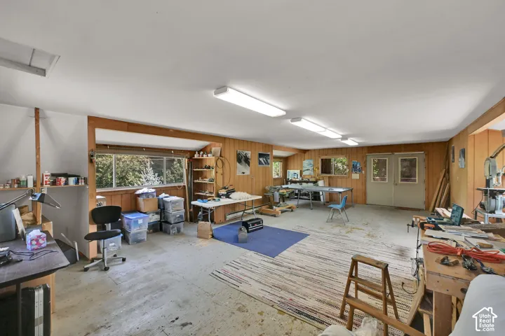 Spacious interior with wood-paneled walls, multiple windows, double doors, and overhead fluorescent lighting
