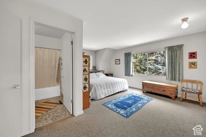 Carpeted bedroom with a large window and an attached bathroom featuring a shower-over-tub combination and mosaic tile flooring